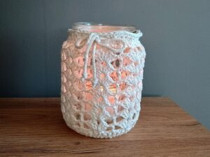 Glas mit gehäkelter Hülle aus cremefarbenem Garn als Windlicht