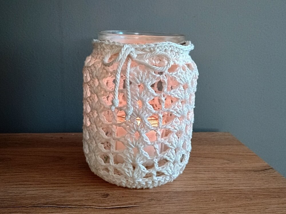 Glas mit gehäkelter Hülle aus cremefarbenem Garn als Windlicht